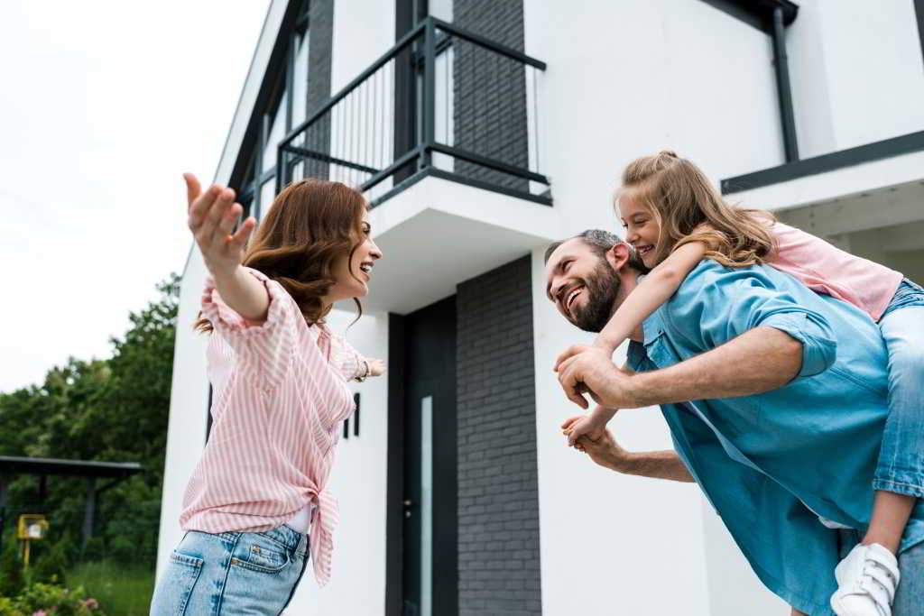 Zu sehen ist eine glückliche Familie vor ihrem Haus