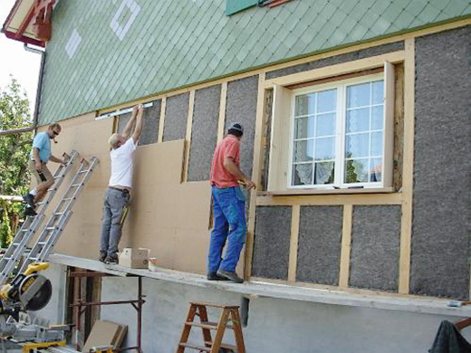 zu sehen sind zwei handwerker die außendämmung an einer fassade anbrinegn.